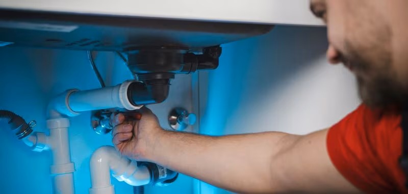Plumber repairing pipework under a sink